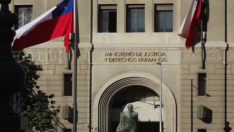 Foto de la parte arriba del arco de la entrada al Ministerio de Justicia de Chile, flanqueado por dos banderas chilenas grandes.