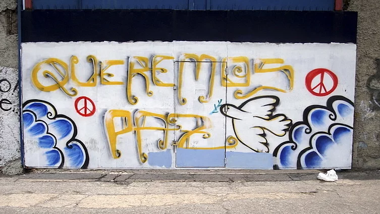 Graffiti en una pared - Queremos Paz escrito en amarillo y con símbolos de paz y una paloma blanca.