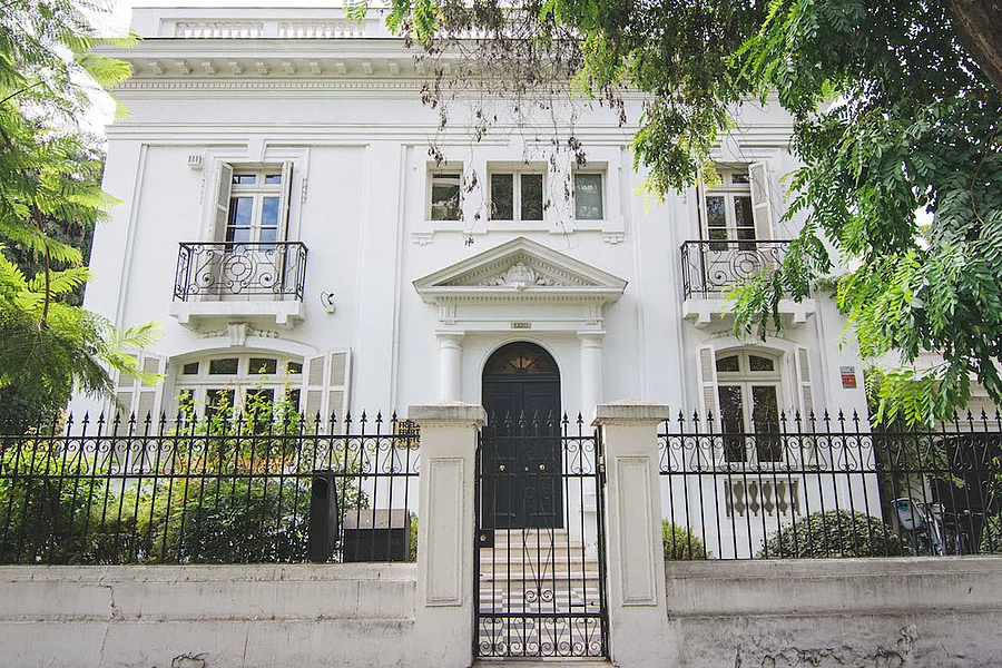 Foto de la casa de la FES Chile. Una casona antigua blanca detrás de unas rejas y arbustos intermedio.